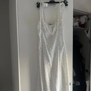 Helt ny!Vit blommig långklänning från NA-KD - Helt ny, aldrig andvänd!! Kvar i förpackningen(råka köpa dubbletter). Nypris 700kr. Säljer en söt vit långklänning från NA-KD med små blå blommor. Klänningen har knytbara axelband, smock i ryggen och en lätt v-ringning med knyt fram. Perfekt för sommarens varma dagar. 