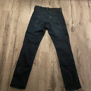 Mörk blå jeansbyxor från Levi's - Säljer ett par Mörkblåa  jeansbyxor från Levi's med klassisk femficksdesign och raka ben. Byxorna har en diskret röd Levi's-lapp på bakfickan och är tillverkade i ett slitstarkt jeanstyg. Perfekta för dig som gillar en tidlös stil. De är 511 och passar slim fit, 32/32