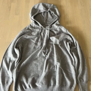 Grå marineull hoodie med luva - En enkel och stilren grå hoodie med huva och dragsko. Tröjan har långa ärmar och ribbade muddar vid ärmslut och nederkant. Perfekt för en avslappnad look. Aldrig använd, kan gå ner i pris vid snabb affär!