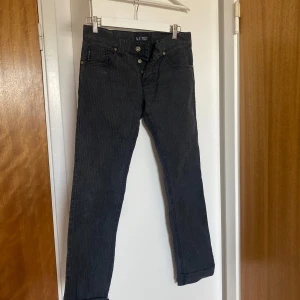 Svarta jeansbyxor från Armani Jeans - Säljer ett par svarta jeansbyxor från Armani Jeans med diskret randigt mönster. Byxorna har raka ben, knappgylf och klassiska fickor. Snygg detalj med Armani-logga på bakfickan. Perfekta för dig som gillar stilrena jeans med exklusiv känsla.