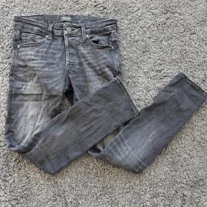 jeansbyxor - Säljer ett par grå/svarta jeansbyxor med slim/glenn passform och klassisk femficksdesign. Byxorna har dragkedjegylf och silverfärgade nitar. Perfekta för dig som gillar en enkel och stilren look. W29,30