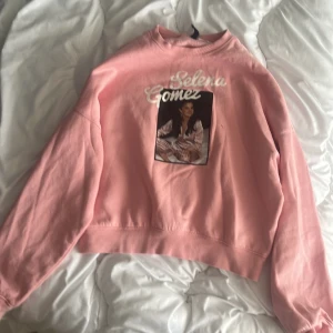 Rosa Selena Gomez sweatshirt från H&M Divided - Säljer en rosa sweatshirt från H&M Divided med tryck av Selena Gomez på bröstet. Tröjan har rund halsringning och långa ärmar. Perfekt för dig som gillar artist-merch och vill ha en mysig och snygg tröja. 🌸