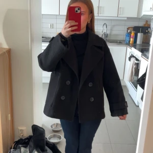 Svart skepparkavaj från Design by si - Stilren svart skepparkavaj från Design by si med dubbelknäppning. Har en liten skada (se bild 3) men är i jackan och man ser inte de när man har på sig den.