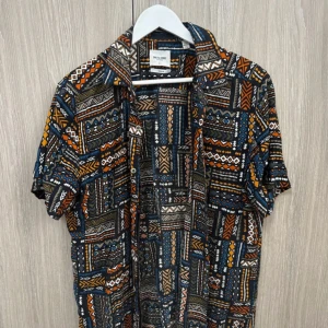 Mönstrad kortärmad skjorta från Only&Sons - Säljer en färgglad skjorta från Only&Sons med korta ärmar och ett unikt, geometriskt mönster i blått, orange, vitt och svart. Skjortan har klassisk krage och knäppning framtill. Perfekt för dig som vill sticka ut med din stil.