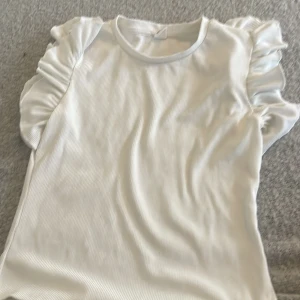 Vit ribbad topp med volangärmar från SHEIN - Supersöt vit ribbad topp från SHEIN med korta volangärmar som ger en extra touch. Perfekt för dig som gillar en enkel men ändå trendig stil. Materialet är mjukt och stretchigt för skön passform.💕