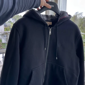 Burberry Hoodie monogram - Schysst burberry hoodie i svart med burberry monogrammet längs hela insidan som syns när man har öppen dragkedja. Såklart äkta, köpt från vongrevencloset. 
