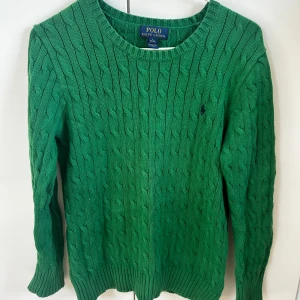 Grön stickad tröja från Polo Ralph Lauren - Säljer en grön stickad tröja från Polo Ralph Lauren med klassiskt kabelstickat mönster. Tröjan har rund halsringning och långa ärmar. Perfekt för dig som gillar stilrena och tidlösa plagg. Köpt för 1999 kr på kidsbrandstore, säljer för endast 399 (STEAL). Storlek 14-16 år, passar mig som bär S-M. Nyskick, inga defekter alls och använd fåtal gånger. Hör av dig för fler frågor eller bilder! 🤩
