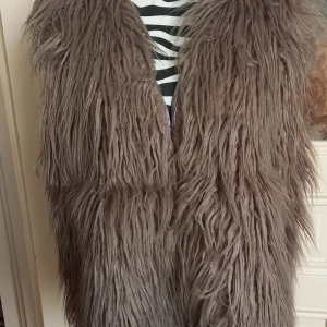 Brun långhårig pälsväst från Rich & Royal - Säljer en brun långhårig pälsväst från Rich & Royal. Västen har en riktigt fluffig och voluminös look, perfekt för att sticka ut. Tillverkad av 80% polyakryl och 20% polyester med ett mjukt foder i 100% polyester.