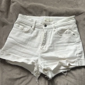 Vita jeansshorts från H&M - Säljer ett par vita jeansshorts från H&M med fransiga kanter och klassisk femficksdesign. Perfekta för varma dagar och enkla att matcha med olika toppar.