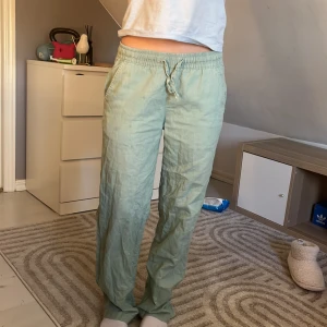 Ljusgröna linnebyxor med dragsko - Säljer ett par ljusgröna linnebyxor med avslappnad passform och dragsko i midjan. Byxorna har raka ben och sidfickor, perfekta för en chill och bekväm stil.