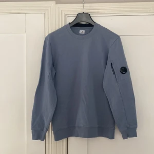 Ljusblå sweatshirt från C.P. Company - Säljer en ljusblå sweatshirt från C.P. Company.             8/10 skick, nån liten repa på själva cp company märkte på amren. Annars väldigt bekväm och stilig. Passform XL, passar även L