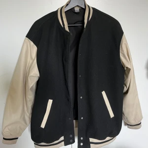 Svart och beige bomberjacka  - Säljer en svart och beige bomberjacka från H&M. Jackan har svarta paneler på fram- och baksida, beigea ärmar och detaljer samt randig krage och muddar. Stängs med tryckknappar och har två fickor framtill. Passar xs-m, knappt använd💗