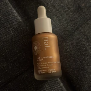Pai The Impossible Glow Hyaluronic Bronzing Drops - Flytande bronzerdroppar med hyaluronsyra från Pai. Kommer i en glasflaska med pipett och har en varm, bronsig ton som ger glow till huden. Passar känslig hud och är vegansk.