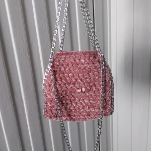 Rosa virkad väska med kedja - Superfin rosa virkad väska med silvrig kedja. Väskan har en mjuk och fluffig känsla och är perfekt för att ge outfiten en söt touch. Liten och smidig att bära med sig till vardags eller när du vill sticka ut lite extra.