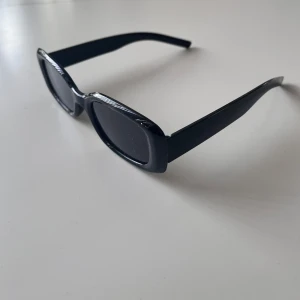Snygga svarta solglasögon - Snygga svarta solglasögon med rektangulära bågar och mörka glas. Glasögonen har en stilren och modern design med breda skalmar. Perfekta för att ge en cool touch till din outfit😎