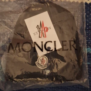 Svart ribbad mössa från Moncler - Säljer en svart ribbstickad mössa från Moncler med klassisk broderad Moncler-logga framtill. Mössan har uppvikt kant och är tillverkad i ett mjukt material som passar perfekt för kyliga dagar.