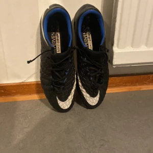 Svarta Nike fotbollsskor med vita detaljer - Säljer ett par svarta hypervenoms. Med storlek 42,5. Använda några gånger max 5. Är i okej skick. Finns ett litet små fel men skon. Men det är fortfarande i okej skick. Pris kan diskuteras.