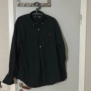 Svart skjorta från Ralph Lauren - Säljer en stilren svart skjorta från Ralph Lauren i ett toppen skick knappast blivit använd pågrund av att den blivit för stor Inga fläckar eller hål köpt i butik för 1500kr. Tveka inte höra av dig vid fler funderingar!