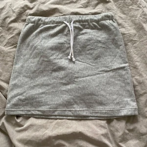 Grå kortkjol  - Säljer en enkel och mjuk grå kortkjol med vit dragsko i midjan. Kjolen har en rak passform och är tillverkad i bomullsmaterial, perfekt för en avslappnad stil. Saknar lapp, men passar XS/S. 