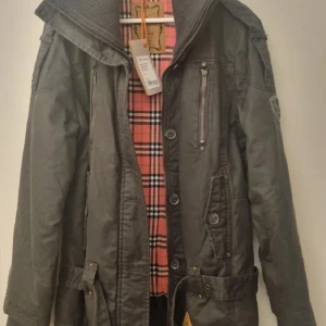 Jacka från Alife & Famous  - Jacka från Alife & Famous med rutigt foder på insidan. Jackan har dragkedja och knappar framtill, samt en hög krage. 