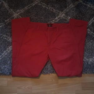 Röda Chinos från Filippa K - Säljer ett par stilrena röda Chinos från Filippa K. Byxorna har normal passform, bälteshällor och klassisk design. Perfekta för dig som vill addera lite färg till garderoben.