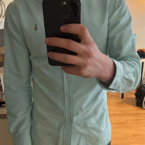 Ljusblå skjorta från Ralph Lauren - Säljer en klassisk ljusblå skjorta från Ralph Lauren med broderad logga på bröstet. Skjortan har knappar framtill och långa ärmar. Perfekt för dig som gillar stilrena och tidlösa plagg.