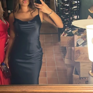 Mörkblå satinklänning med smala axelband - Säljer en elegant mörkblå satinklänning med smala axelband och lätt draperad urringning. Klänningen har en figurnära passform och är perfekt för speciella tillfällen.