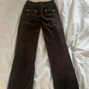 Svarta helt nya juicy couture mjukisbyxor - Svarta mjukisbyxor med bred resår i midjan och snörning framtill. Byxorna har två stora fickor fram och två fickor bak med knappdetaljer. Perfekta för en avslappnad stil.