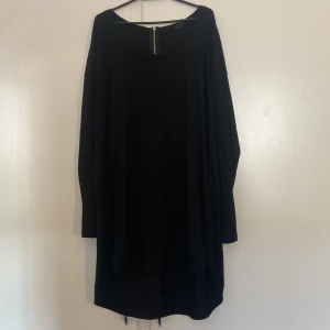 Svart långklänning från Gina Tricot - Svart långklänning från Gina Tricot i mjukt material med rund halsringning och lång ärm. Klänningen har en snygg dragkedja i nacken som detalj och en loose passform som ger en chill vibe. Perfekt för dig som gillar enkel och stilren look.