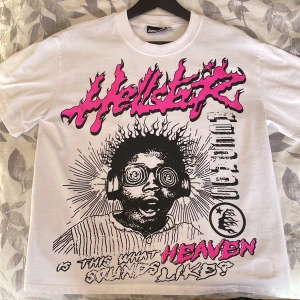 Hellstar vit grafisk t-shirt S - Säljer en vit t-shirt från Hellstar med fet grafisk print i svart och neonrosa på både fram- och baksidan. Trycket har eldiga bokstäver och coola detaljer, och materialet är 100% bomull. Perfekt för dig som gillar streetwear med attityd.