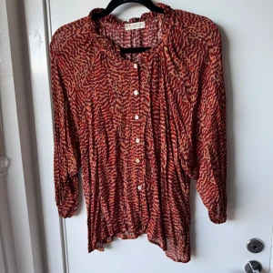 Röd leopardmönstrad blus Stank Stockholm  - Säljer en luftig och snygg blus från Stank Stockholm med leopardmönster i rött och beige. Skjortan har långa ärmar, knappar framtill och en liten volang vid kragen. Perfekt för dig som gillar att sticka ut med coola mönster.