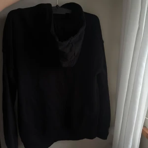 Svart hoodie från Wai Wai - Svart hoodie från Wai Wai med klassisk huva och stor magficka framtill. Tröjan har långärmade ärmar och är gjord i mjuk bomull. Endast använd max 5ggr, och inga defekter. Läs gärna bio! OBS skriv innan köp, säljer på fler ställen!❤️