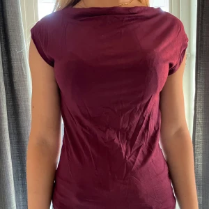 Båtringad vinröd topp kortärmad - Snygg vinröd topp med korta ärmar och rundad hals. Modellen är slim och sitter nära kroppen, perfekt för dig som gillar en enkel men stilren look. Materialet är mjuk bomull som känns skönt mot huden. Passar dig som vill ha en basic topp med lite färg. Strl xs men passar även s