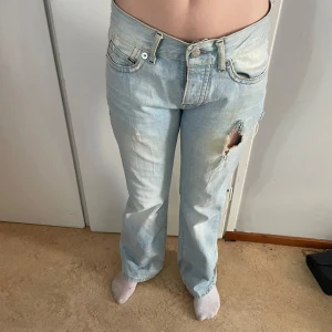 Ljusblå Crocker jeans med hål - Säljer ett par ljusblå jeans från Crocker med låg midja och rak passform. Jeansen har slitna detaljer och ett stort hål på låret samt fransiga kanter vid bakfickan. Klassisk femficksmodell med knapp och dragkedja framtill. Perfekt för dig som gillar en avslappnad och edgy stil.