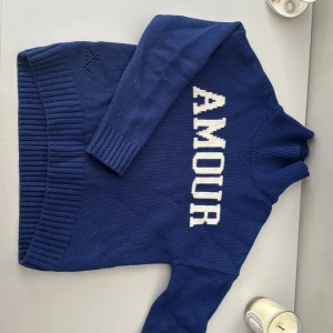 Blå stickad tröja med AMOUR-tryck - Zadig & Voltaire, Snygg blå stickad tröja med vit text 'AMOUR' framtill. Tröjan har ribbade muddar vid ärmslut och nederkant samt långärmad design. Perfekt för dig som gillar statement-plagg och vill ha en mysig, cool look.