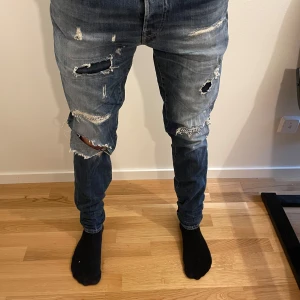 Blå slitna jeans från Jack & Jones - Säljer ett par blå jeans från Jack & Jones med coola slitningar och hål på framsidan. Jeansen har en slim passform och är 32/32