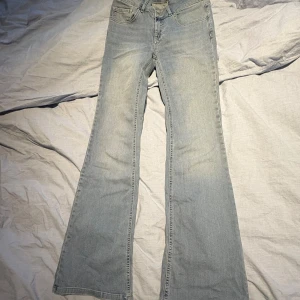 Bootcut jeans från Nelly ljusblå - Säljer ett par ljusblå bootcut jeans från Nelly med klassisk femficksdesign. Jeansen har två knappar framtill och är tillverkade i mjukt denimtyg. Perfekt för dig som gillar retrovibbar och vill ha en snygg siluett.