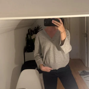 Grå stickad v-ringad tröja - Säljer en chill grå stickad tröja med v-ringad hals och långa ärmar. Perfekt för dig som gillar enkel och clean stil. Tröjan har ribbad kant nedtill och vid ärmslut, vilket ger en snygg detalj. Passar till jeans eller kjol för en avslappnad look.