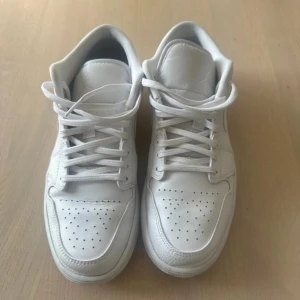 Nike Jordan 1 Low Triple White - Nike Jordan 1 Low i helvit färg med snyggt skinnmaterial och klassisk snörning. Swoosh-loggan på sidan och Jumpman på plösen ger en clean och stilren vibe. Perforerad tå för extra ventilation och platt sula för skön komfort. Perfekt för dig som gillar minimalistisk streetstil. Använda  fåtalgånger 