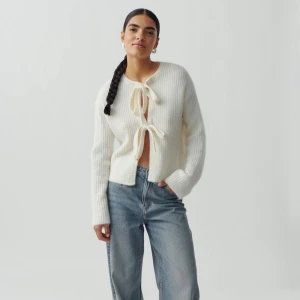 Vit stickad kofta med knyt - Superfin vit stickad kofta med två stora knytband framtill. Koftan har ribbad struktur och långärmad passform, perfekt att slänga över en topp. Tröjan går att ha med knytet både fram och bakåt! 