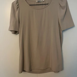 Beige topp från Indiska med puffärm - Snygg beige topp från Indiska med korta puffärmar och rund halsringning. Tillverkad i mjuk bomull som känns skön mot huden. 