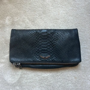 Zadig & Voltaire väska  - Superfin grå/ svart clutch väska från Zadig Voltair. Ett kort och ett långt väskband i metall tillkommer. Nypris ca 4000 kr. Väskan är väl använd med tydliga tecken på användning, därav priset. 