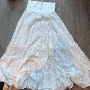 Vit långkjol i bomull från Italien - Säljer en vit långkjol i 100% bomull, tillverkad i Italien. Kjolen har en bred midja och volangdetaljer nedtill som ger en flowy och chill vibe. Perfekt för varma dagar och enkel att styla med sneakers eller sandaler.