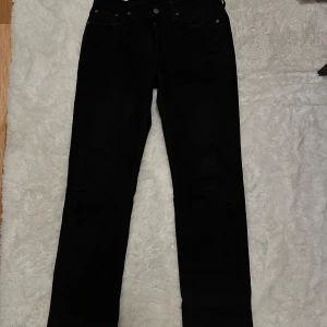 Svarta Levi's Premium jeans W30 L32 - Svarta jeans från Levi's Premium med klassisk femficksdesign och raka ben. Snyggt svart läderpatch baktill och diskreta nitar vid fickorna. Passar dig som gillar stilrena och tidlösa jeans med en clean look. Materialet är slitstarkt och bekvämt.