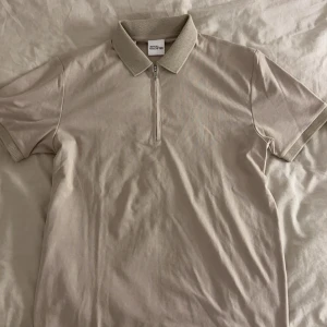 Beige pikétröja från Selected Homme - Snygg beige pikétröja från Selected Homme med klassisk krage i mesh och half zip framtill. T-shirten har korta ärmar och ribbade detaljer vid ärmslut och krage. Perfekt för dig som gillar stilren och enkel design.