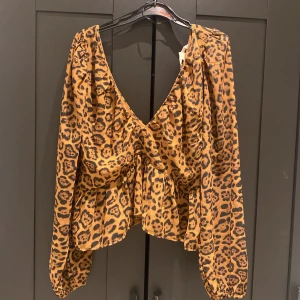 Leopardmönstrad blus från H&M - Säljer en leopardmönstrad blus från H&M i storlek M. Blusen har djup v-ringning, långa puffärmar med resår vid ärmslut och en snygg knytning i ryggen. Materialet är lätt och flowy polyester.