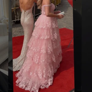 Kemtvättad Rosa balklänning med spets och volanger - Drömmig rosa långklänning med offshoulder och flera lager volanger. Använd en gång på min bal. Köpt på dressroom för 5500 kr. Jag säljer för 4500. Jag har s i storlek på kläder och i denna klänning heter storleken 6