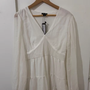 Vit omlottklänning från Boohoo - Säljer en vit kortklänning från Boohoo med v-ringad omlottfront och långa ärmar. Klänningen har volangdetaljer och är tillverkad i ett lätt, transparent tyg som ger en luftig känsla. Perfekt för sommarens alla tillfällen! Passar perfekt för studenten!