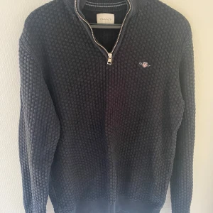 Svart stickad tröja från GANT - Säljer en svart stickad tröja från GANT i storlek M. Tröjan har ett snyggt rutmönster, half zip-dragkedja och broderad logga på bröstet. Hör av dig om du har några frågor :)