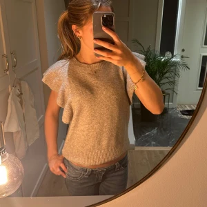 Beige stickad topp med volangärm - Superfin beige stickad topp från LMTD med korta volangärmar och rund hals. Ribbad kant nedtill och vid halsen. I storlek 158/164 men skulle säga att den passar xs/s.